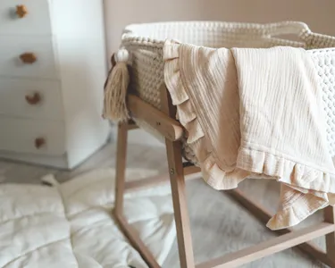 Empty baby bassinet with a light, soft blanket draped over the side, in a cozy room.